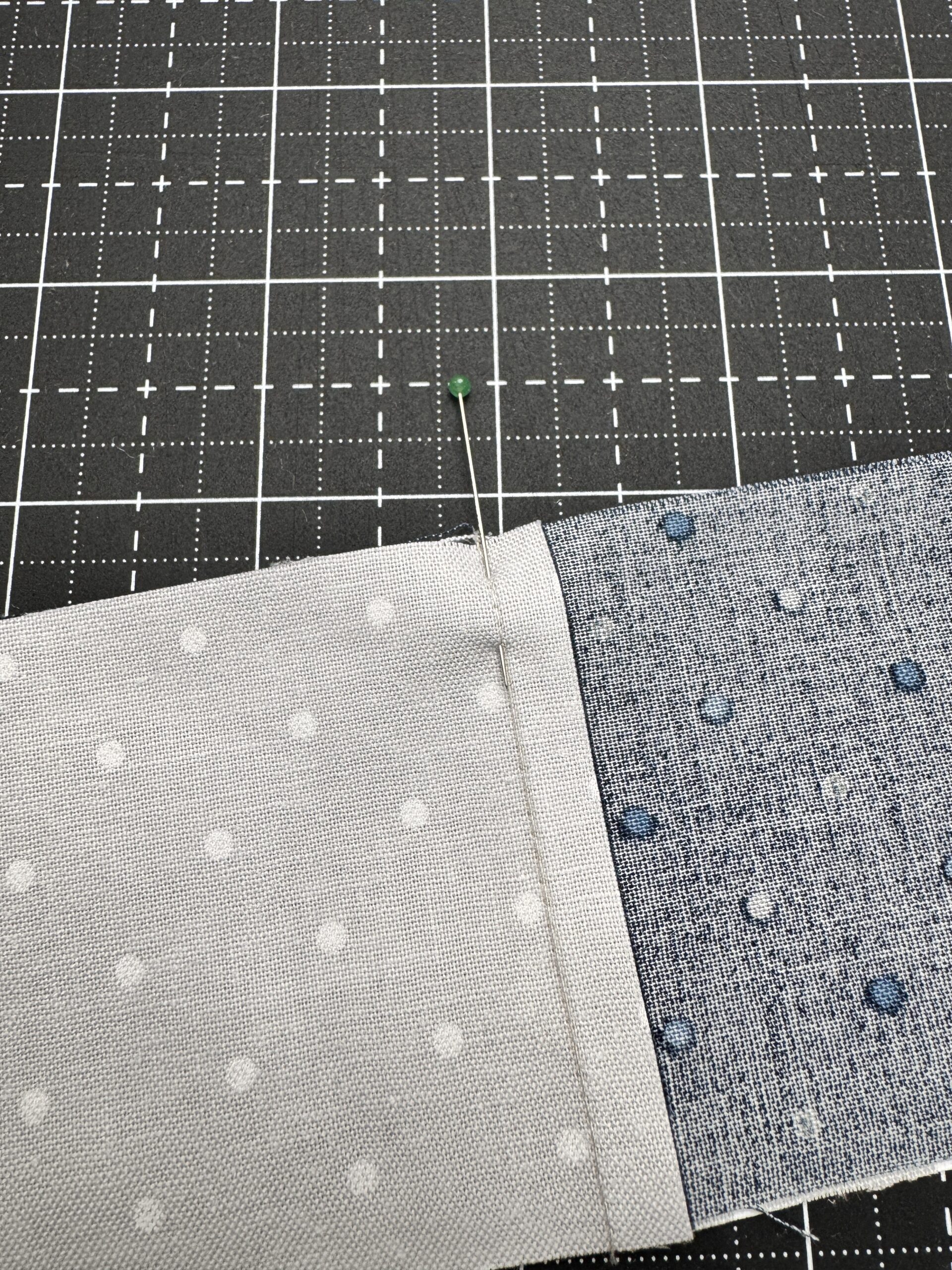 Close-up of a pin placed through the nested seam intersection of a four patch unit to hold alignment before sewing