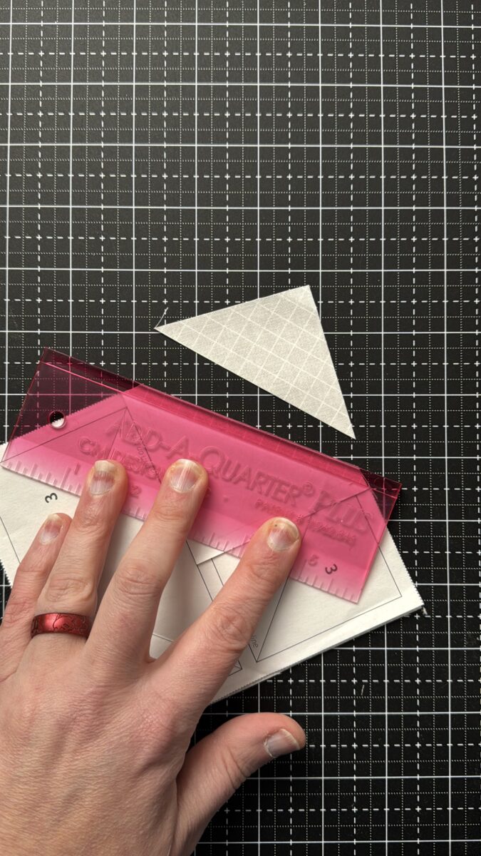 Trimming fabric for placement two using an add a quarter ruler on foundation paper pieced flying geese