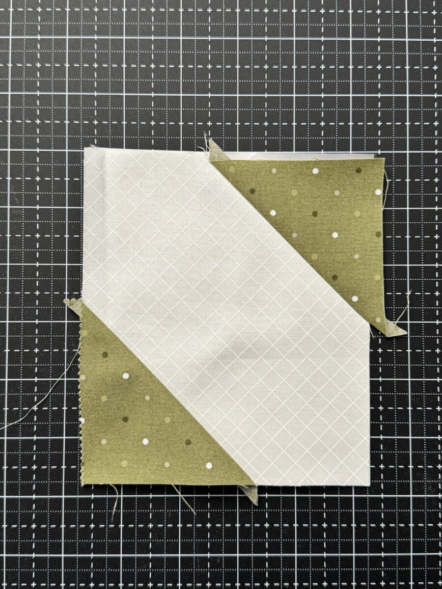 First two side triangles sewn onto foundation paper for flying geese unit