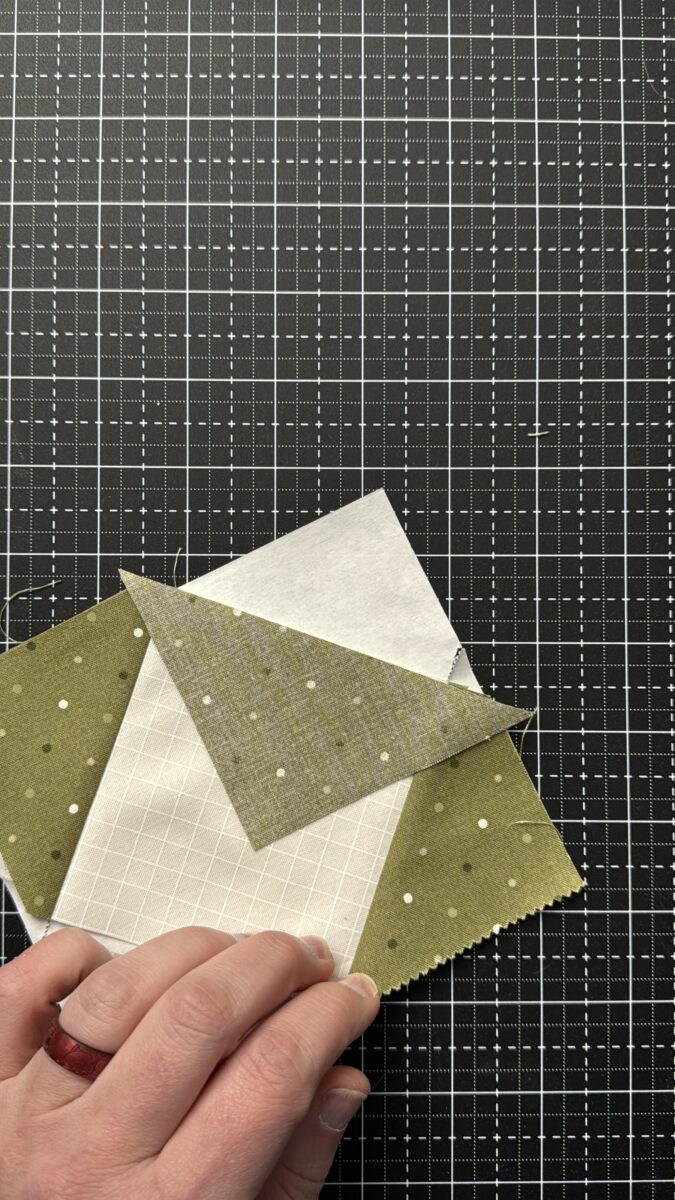 Aligning fabric piece three along trimmed edge of foundation paper before sewing flying geese unit
