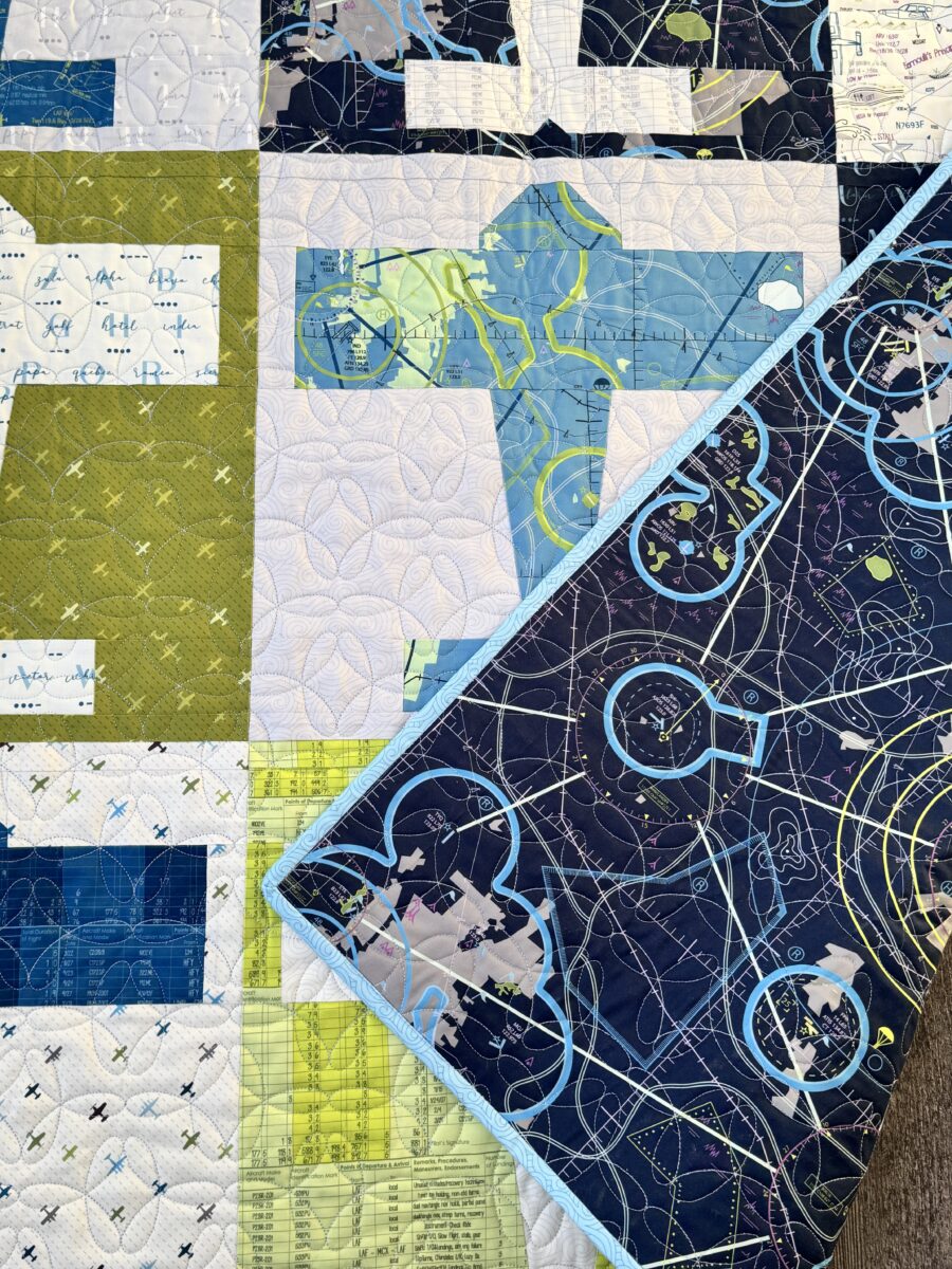 Aviator quilt corner folded over showing navy flight map backing fabric layered over airplane quilt front