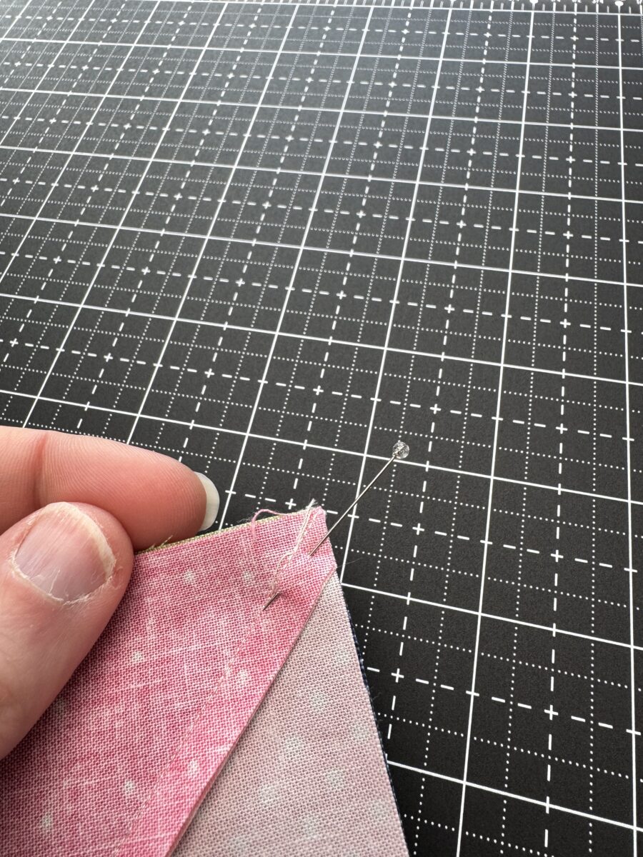 Two half square triangle units nested together with a pin placed through the corner intersection to hold alignment before sewing