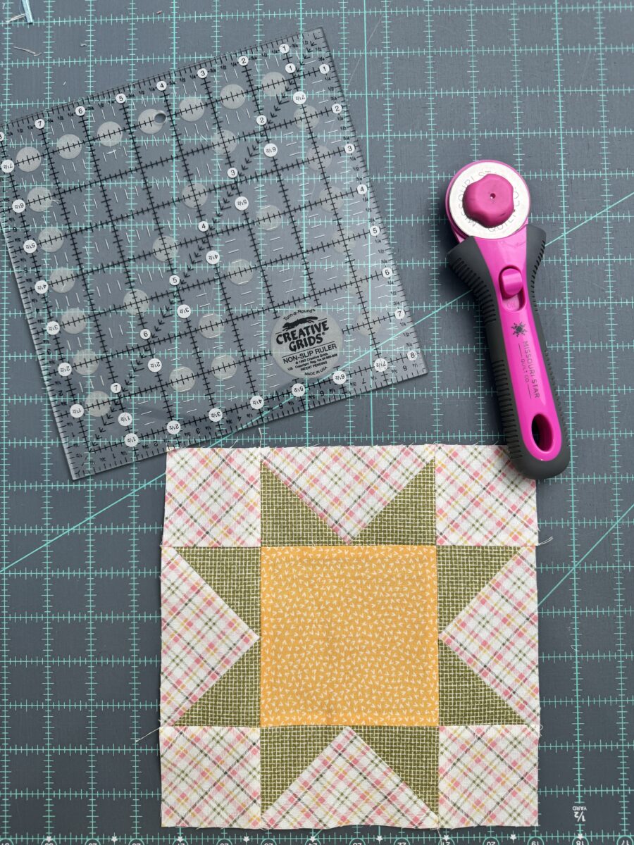 Flat lay of Star quilt block, rotary cutter, and 8.5 inch square ruler on cutting mat