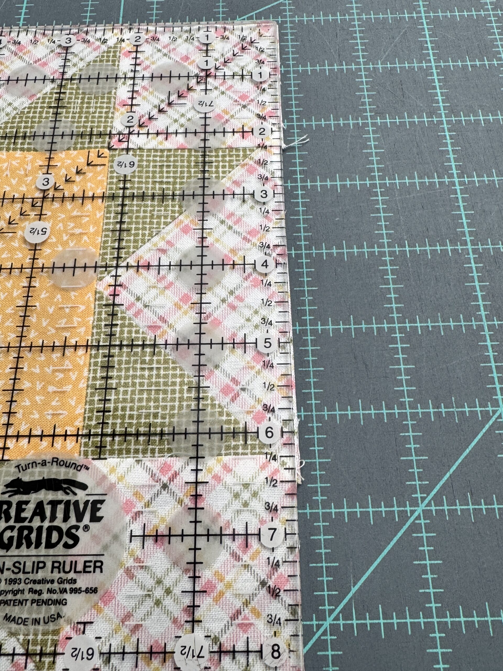 Showing the edge of the ruler on the edge of the quilt block and the slight excess fabric that needs cut off while trimming quilt blocks for accuracy