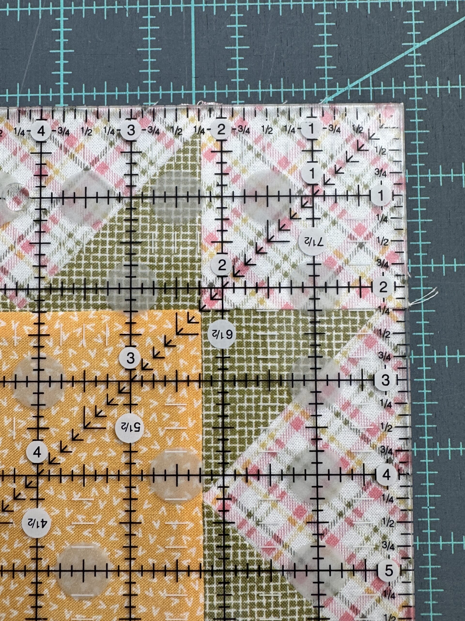 Using the measurement lines on the quilt ruler aligned with two cross seams on a quilt block while trimming quilt blocks