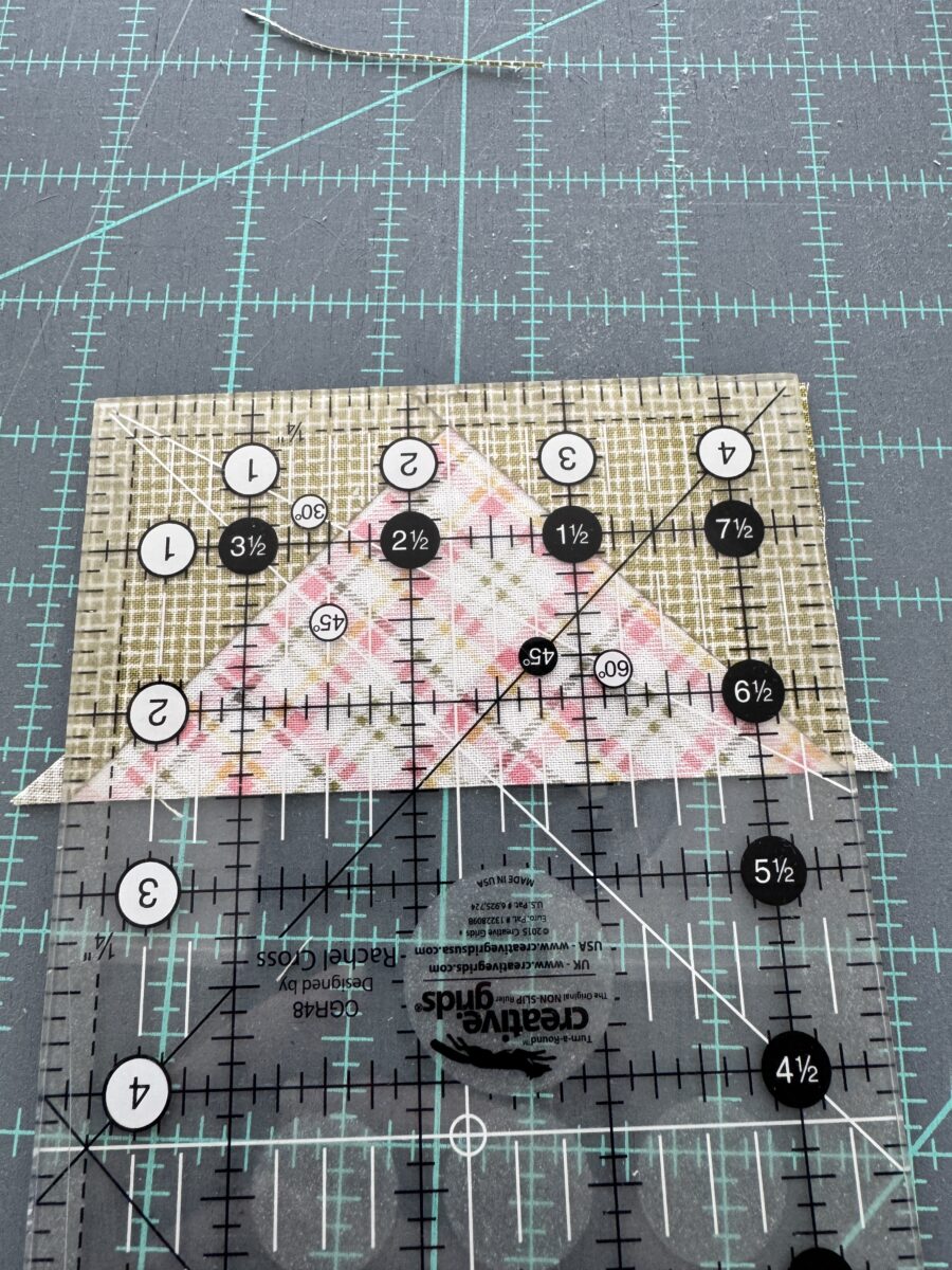Ruler aligned on flying geese unit using the center line on the point of the unit to trim the two short sides.