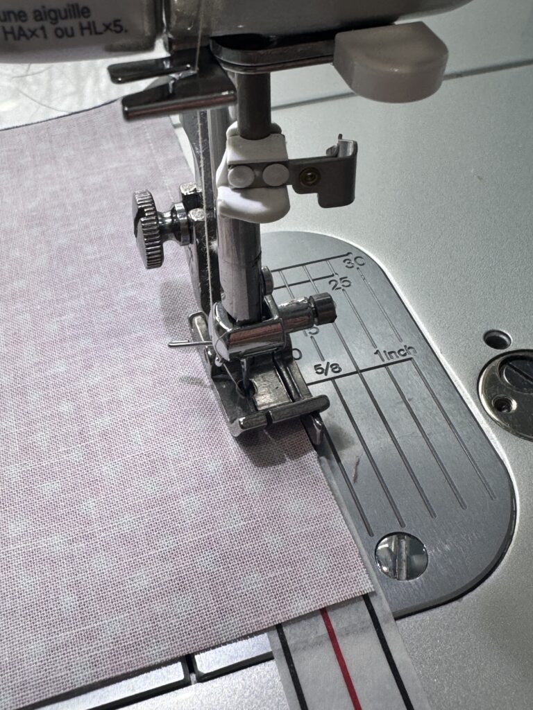 Close-up of sewing with a 1/4 inch presser foot guiding fabric along a seam guide