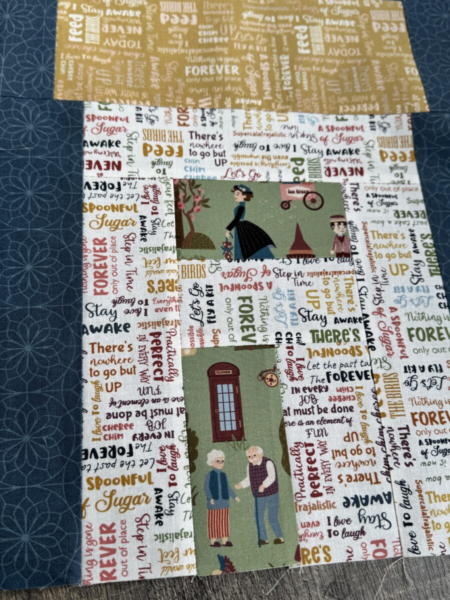 Close up of house quilt block with multicolored text fabric, green print window and door, and kite above roof