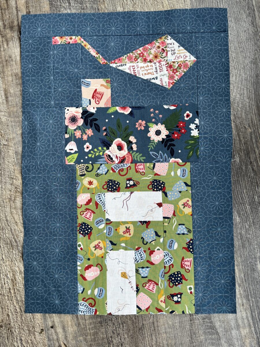 House quilt block with green teapot print, white kite window and door, and pink and white kite above roof