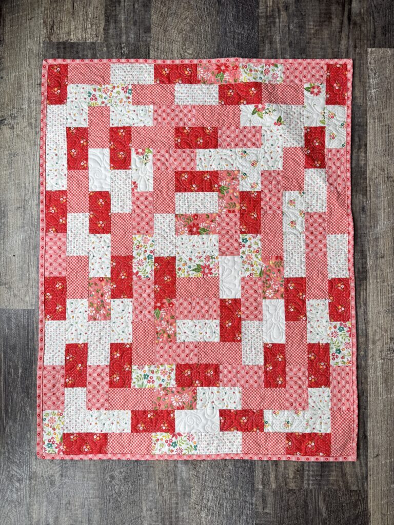 Scrappy pink, white, and red potato chip quilt made with identical rectangles in rows around a center set of strips.