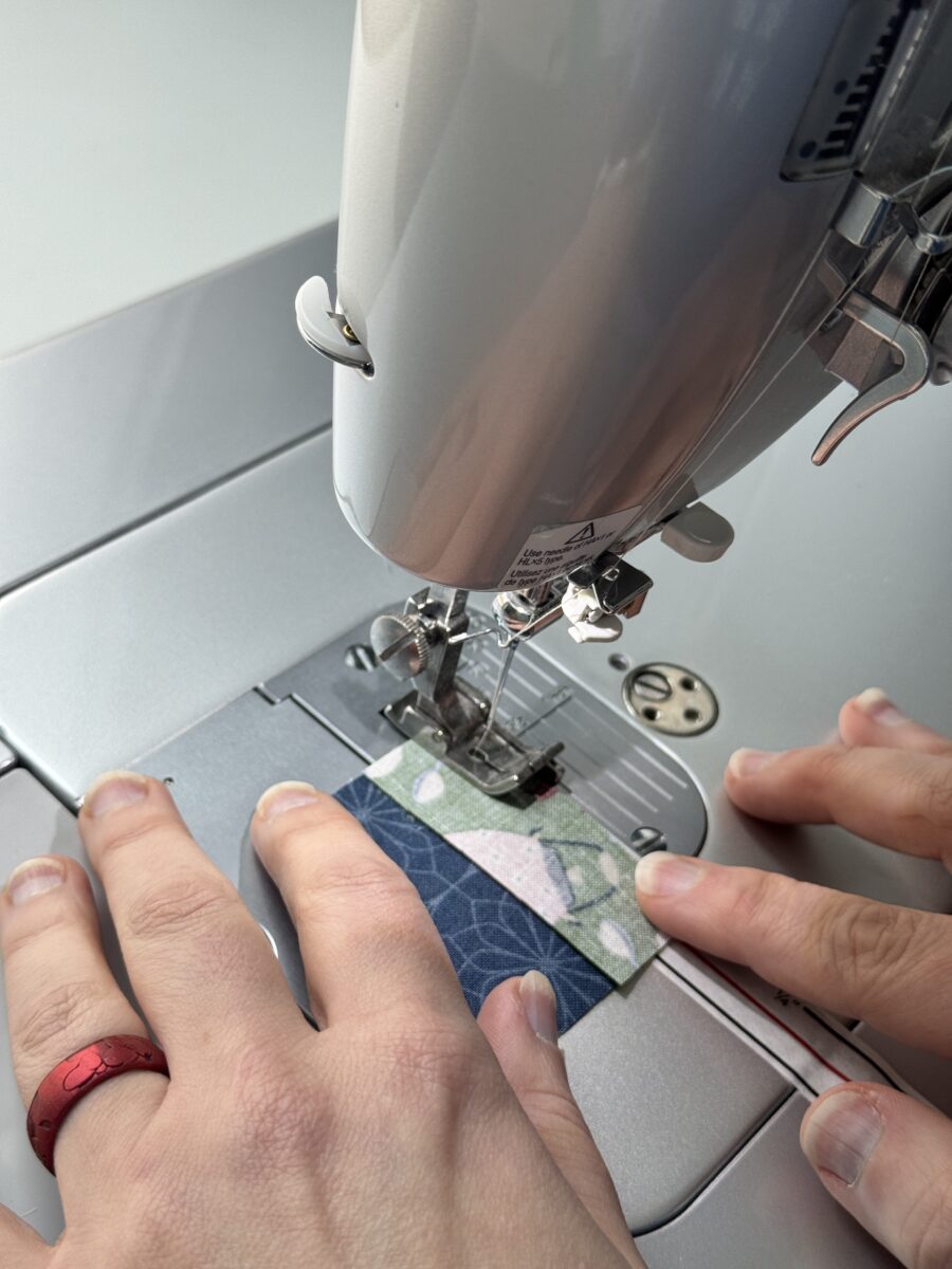Hands lightly guiding fabric through a sewing machine without pulling or pushing to maintain a straight seam