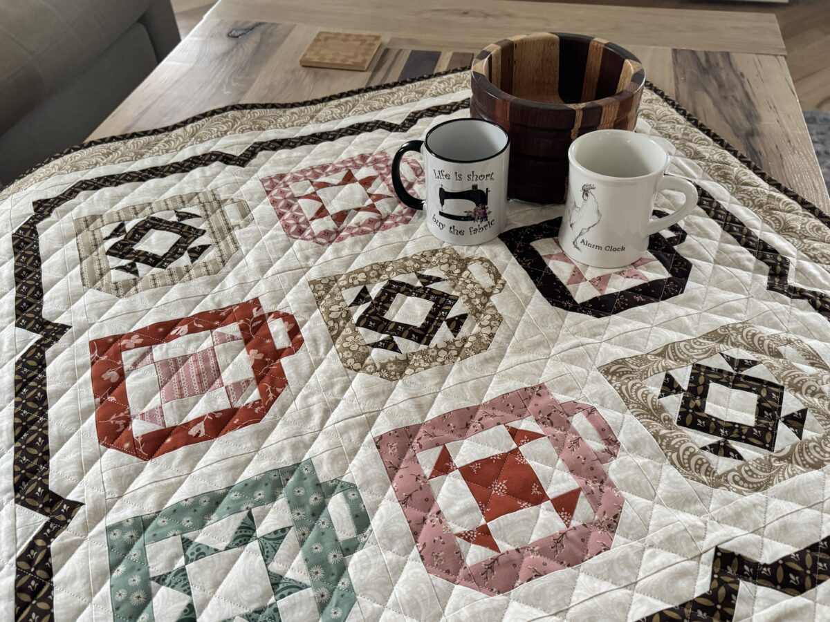 Coffee mug quilt made with Morning Latte fabric displayed on a coffee table with two mugs and a wooden bowl