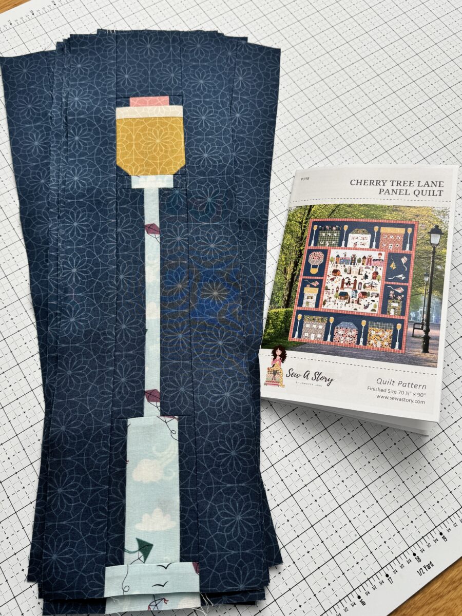 Stack of eight finished lamppost quilt blocks next to Cherry Tree Lane quilt pattern