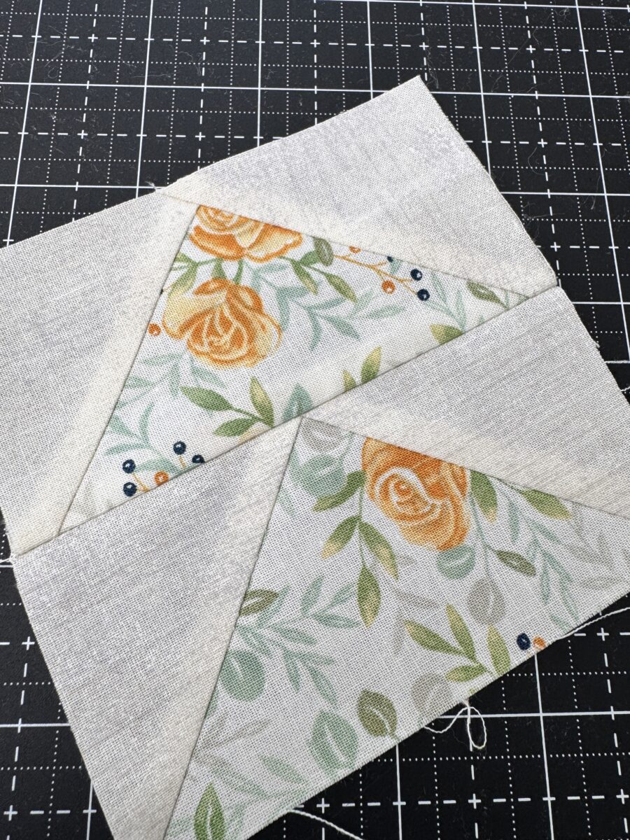 Two flying geese units sewn together and pressed open with points aligned at the seam