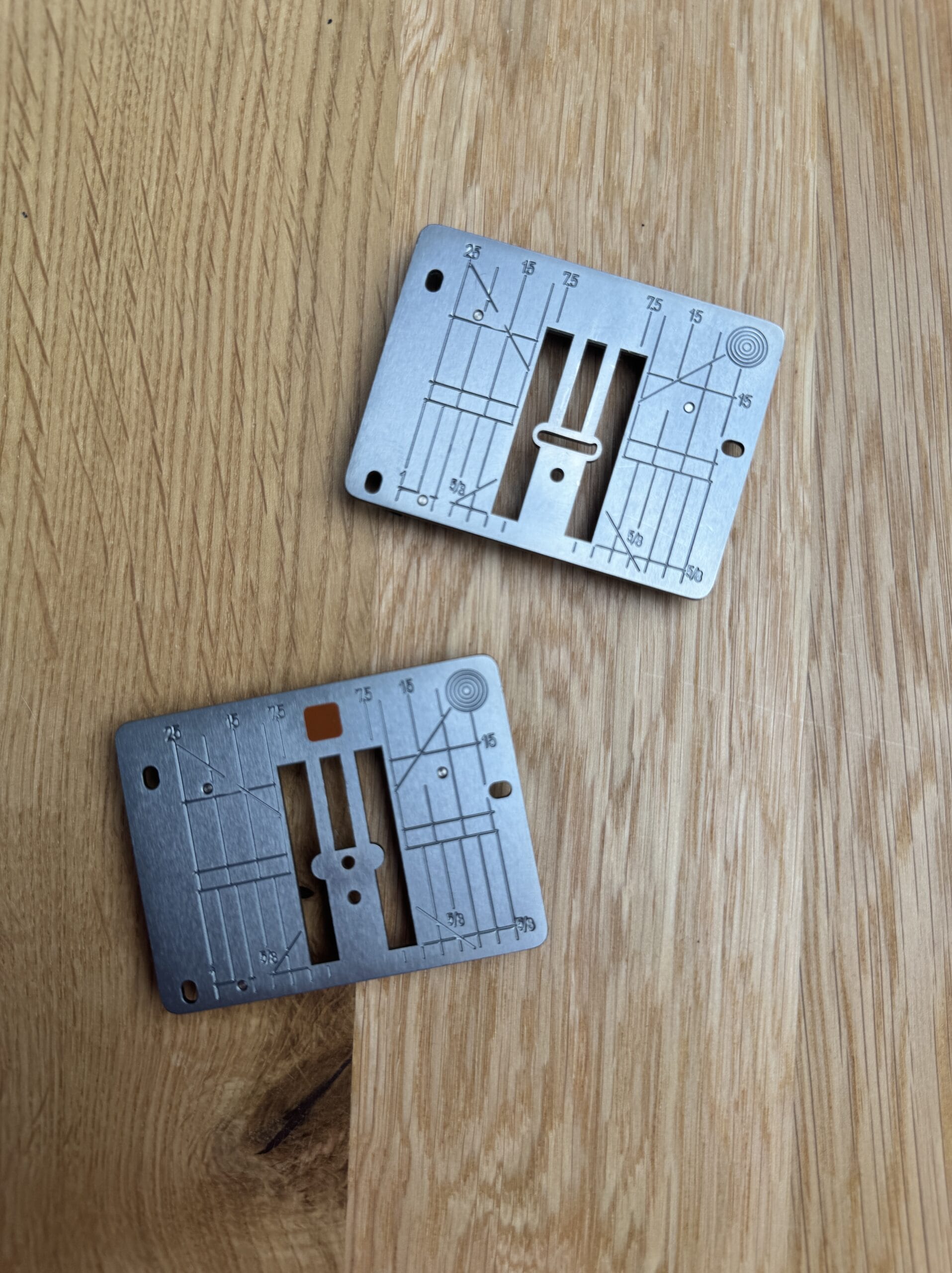 Two needle plates from a Bernina sewing machine. one with a single hole and one with a wider hole for decorative stitches.