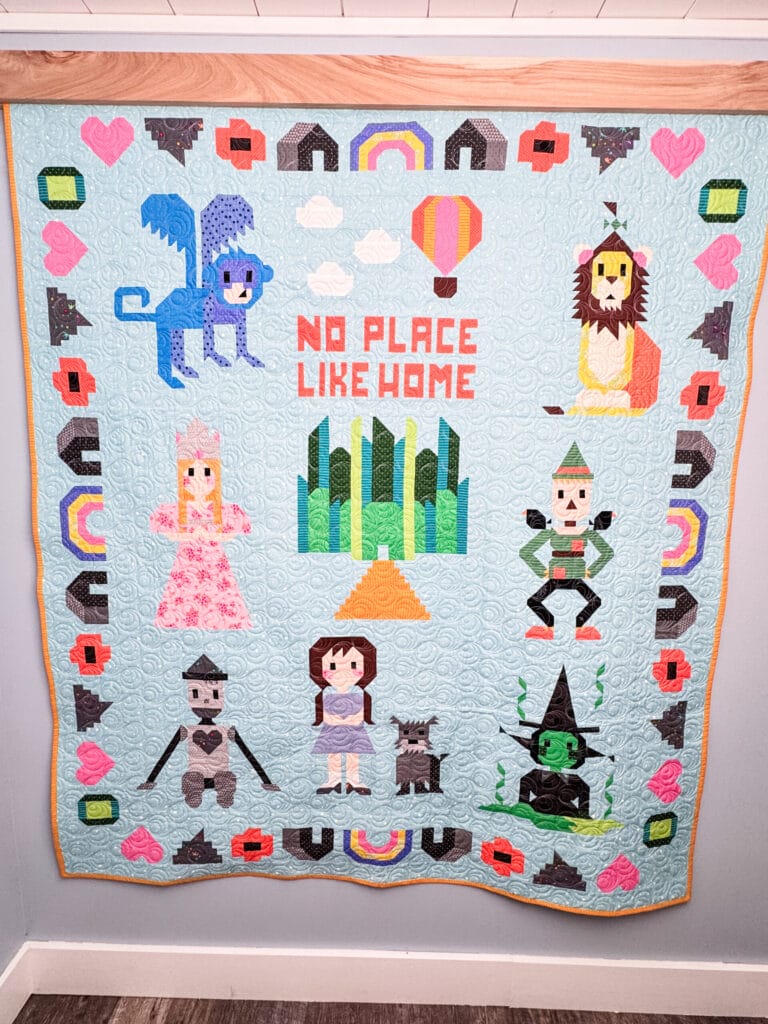 Completed Sew Place Like Home quilt featuring characters from Wizard of Oz including tin man, Dorothy, the cowardly lion and more.