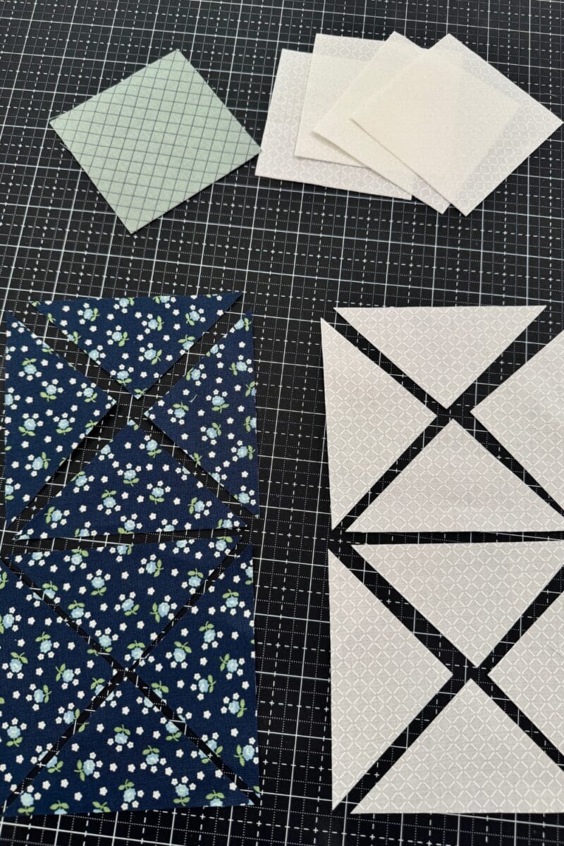 The individual fabric pieces needed for the Ohio star quilt block including a center square, four corner squares, and four oversized squares cut twice on the diagonal in contrasting colors.  