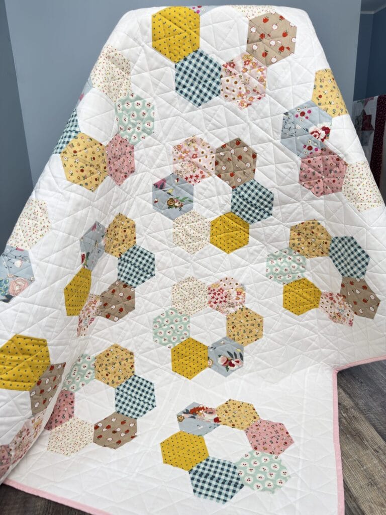 Finished Hexie Blooms quilt draped over a chair