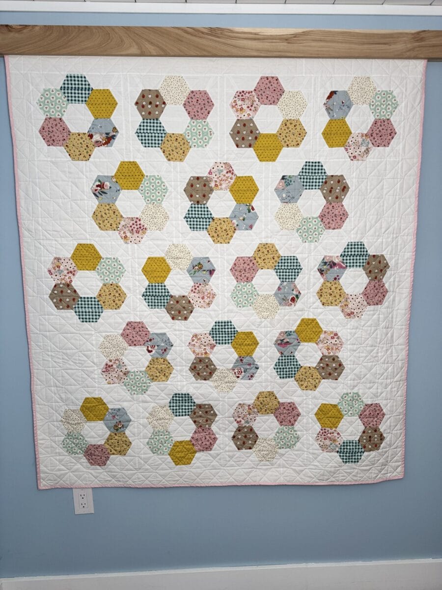 Finished Hexie Blooms throw quilt hanging on a wall