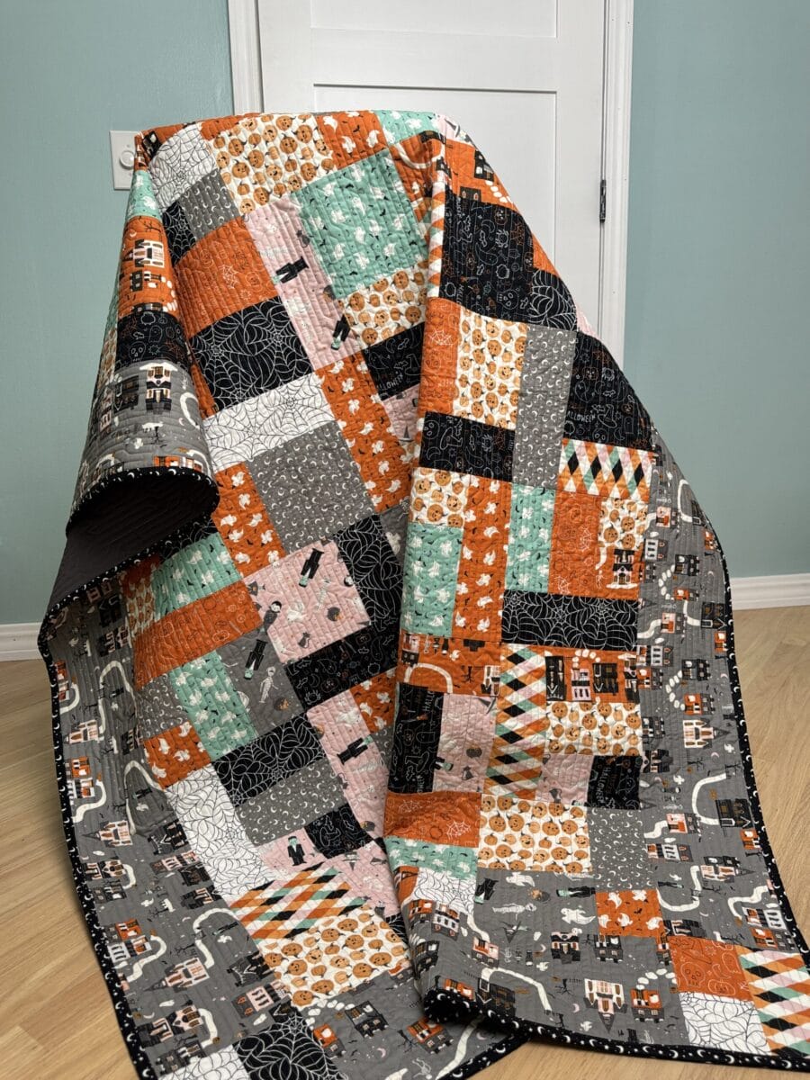Finished Halloween quilt made with Frank & Friends fabric draped over a chair