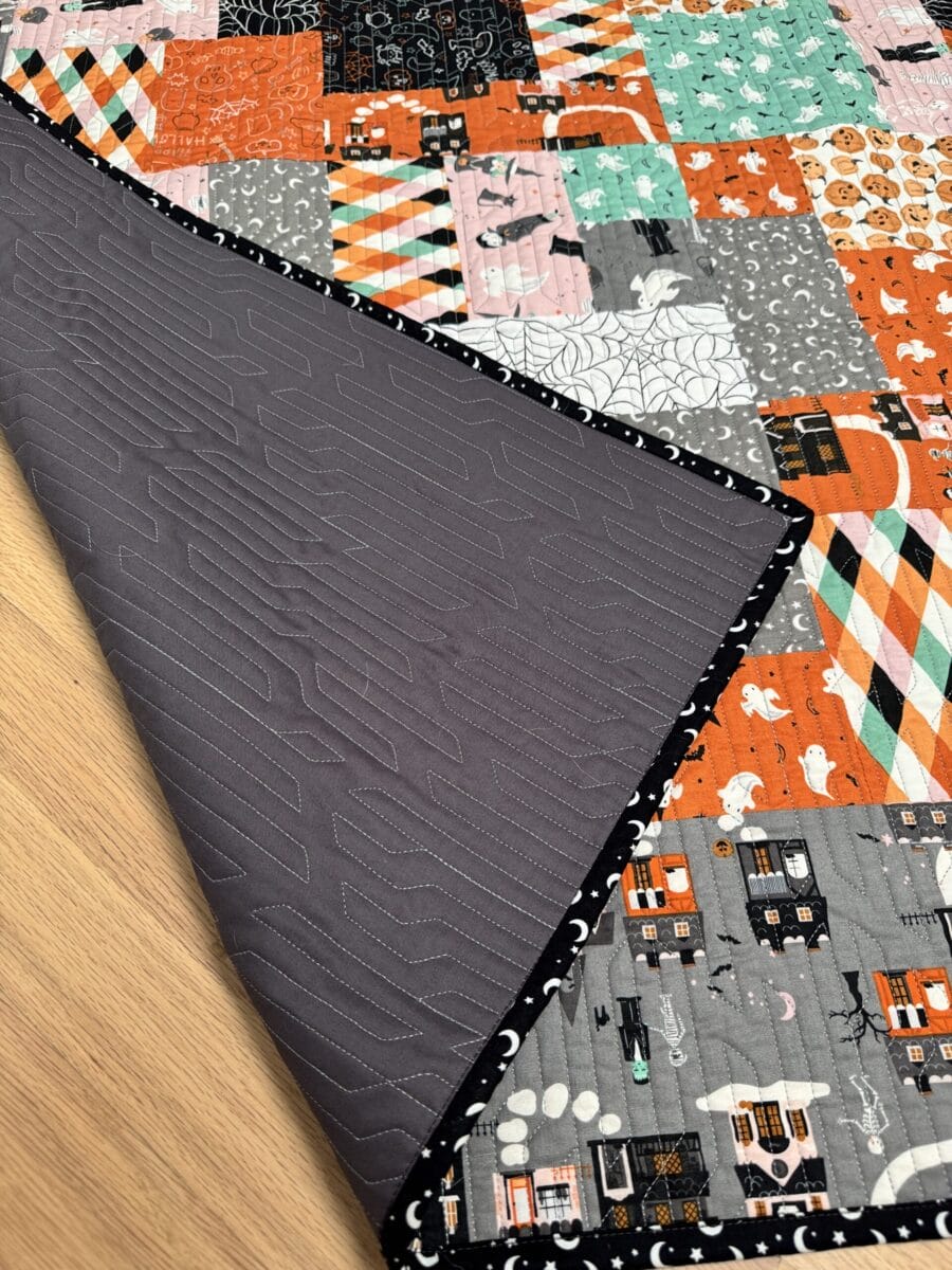 Corner of Halloween quilt flipped over to show the charcoal gray backing and quilting