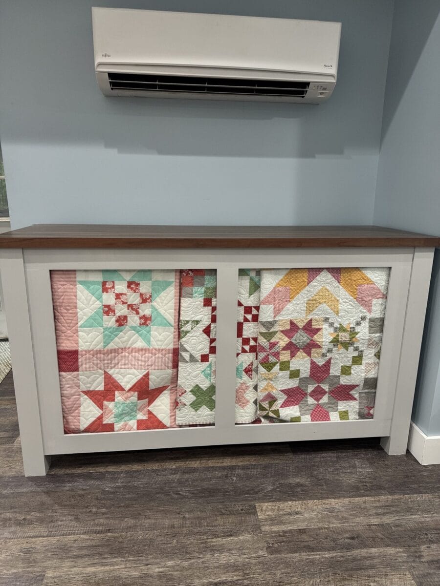 Quilt cabinet displayed against a wall with three different quilts showing through the front glass.  