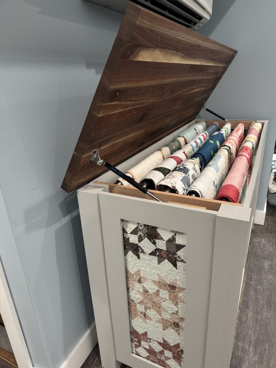 Quilt display cabinet with top that opens up to display rods of quilts inside