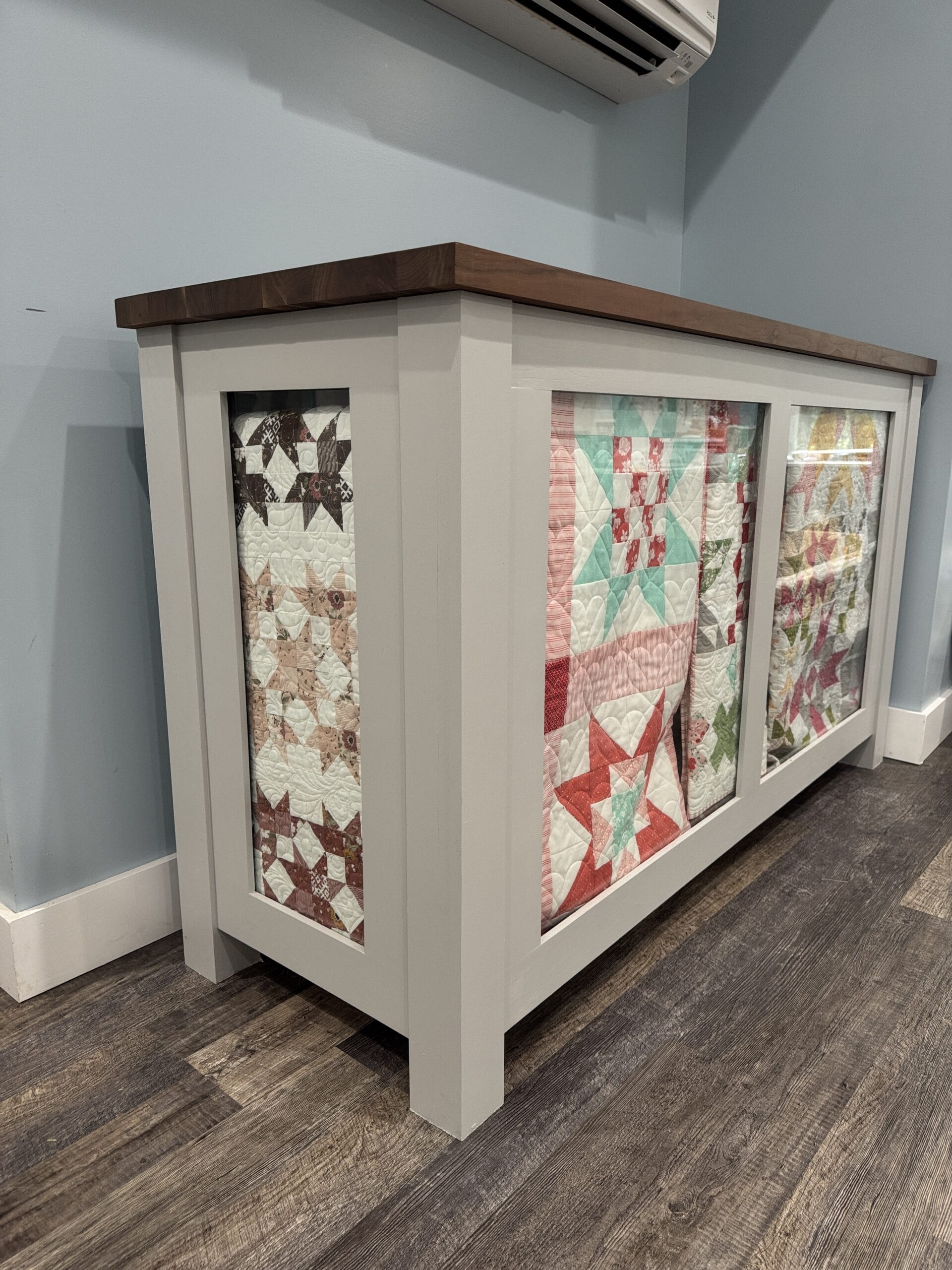 Side view of the DIY quilt cabinet build showcasing a quilt through the glass on the end and multiple quilts on the front glass display.